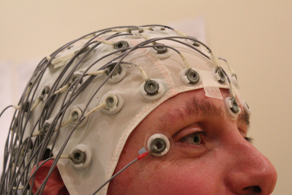 Photo of the upper half of a man's head is shown. He's wearing a mesh fabric cap with multiple electrodes connected to it. The photo title is 