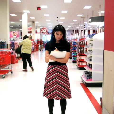 A woman holding and writing in a notebook stands inside a Target store. Other shoppers are in the background.