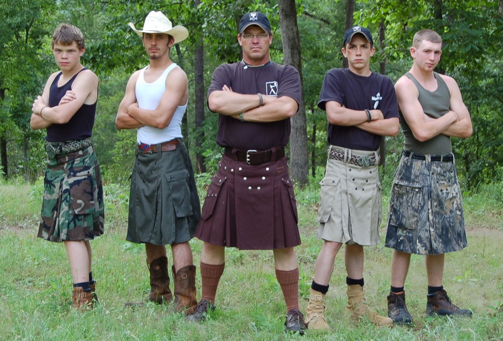 Five men wearing utilikilts and facing the camera, their arms crossed in front of their chests.
