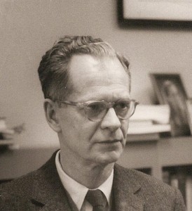 B. F. Skinner, looking away from the camera, wearing glasses and a suit and tie.