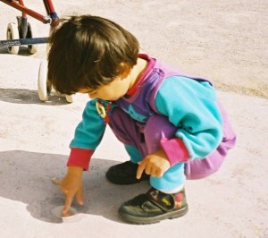 A young child plays with their finger in the dirt.