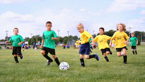 Children playing soccer. A green team and a yellow team, both boys and girls, run towards the ball.