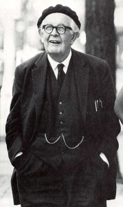 Jean Piaget standing, smiling, wearing a 3-piece suit and a beret.
