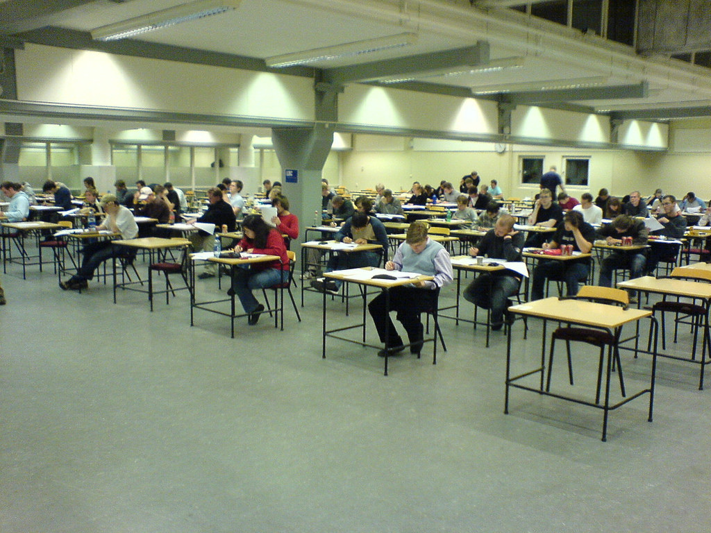 Photo of a room full of students seated at individual desks taking an exam.