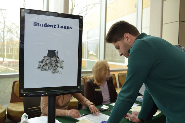 A male student leans over a table with a sign on it that reads, 