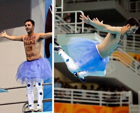 A shirtless man wearing a tutu and polka-dotted tights leaps off a diveboard. The words GoldenPalace.com 2004 are painted on his bare chest.