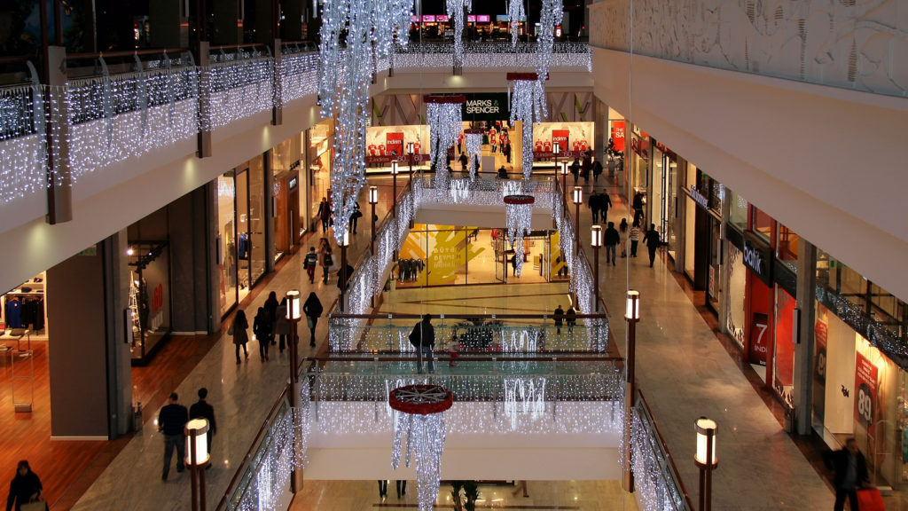 Photograph of a shopping mall. The photograph is taken from the third floor of the mall, and the second and first floor can be seen, as the center of the mall is open and bridged with walk ways. The mall is decorated for winter, and lights hang from the balconies of the third and second floors.