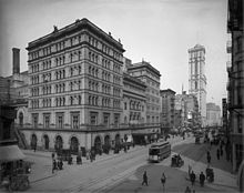 A tall, imposing stone building in an almost empty city street with tramcar passing. A tower in the background is the only other highrise building.