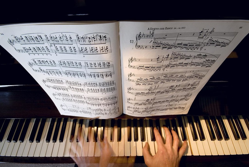Photo of piano keyboard: two hands are shown along with sheet music instructing the pianist to play 