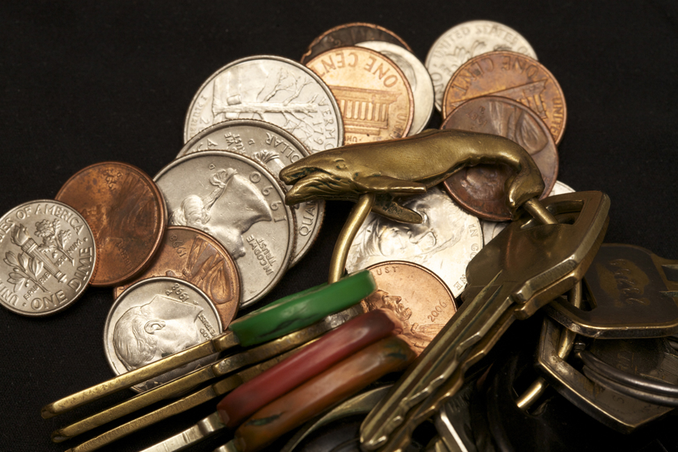 This is a photo of change a set of keys in a pile. There appear to be five pennies, three quarters, four dimes, and two nickels. The key ring has a bronze whale on it and holds eleven keys.