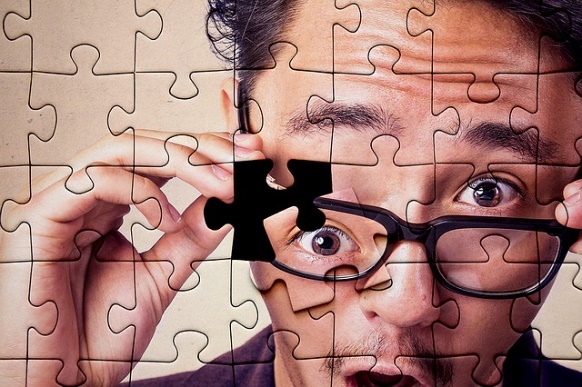 picture of a man with glasses stylized as a puzzle board. his eye is one of the missing pieces. 