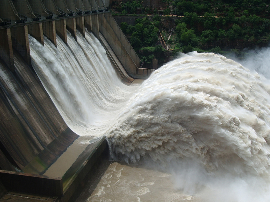 A large volume of water gushes out of the gates of a dam at a hydroelectric facility.