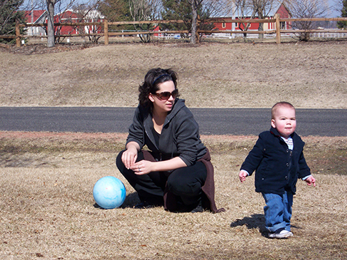 A photograph shows a person squatting down next to a small child who is standing up.