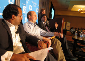 Three people sitting in chairs on a stage while another person stands at a podium