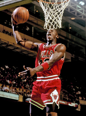 Michael Jordan in the air about to through the basketball through the hoop