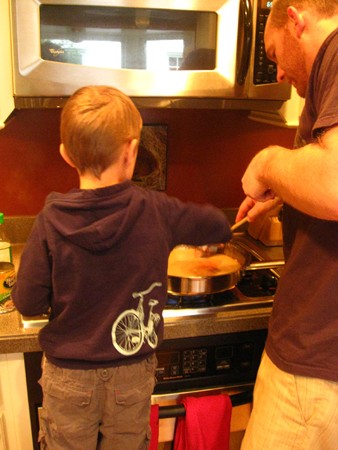 A woman and young boy in the kitchen frosting cookies.