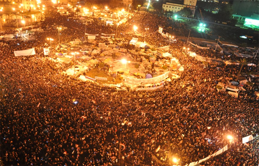 Photo of a crowded Tahirir Square in Cairo, Egypt where many people in the crowd are waiving Egyptian flags in the air