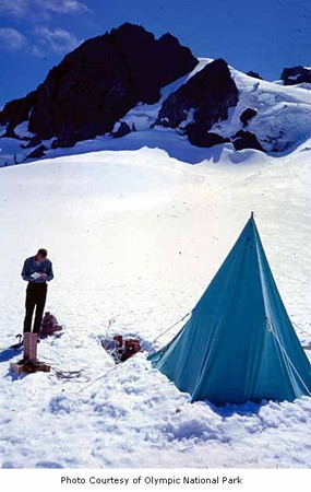 A man is shown taking notes outside a tent in the mountains.
