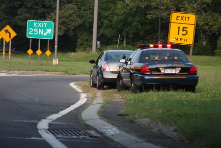 The image shows a state police car that has pulled over another car near a highway exit.