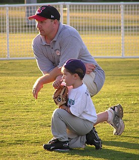 This image is of a kneeling man with a small child who is learning to play baseball.