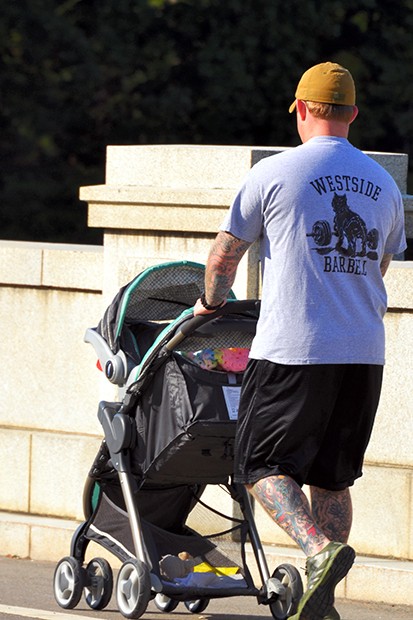 A photo of a man with many tattoos on his legs, pushing a baby stroller outside