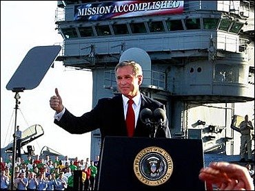 Photo of President George W. Bush giving the thumbs-up sign with a large sign in the background that reads, 