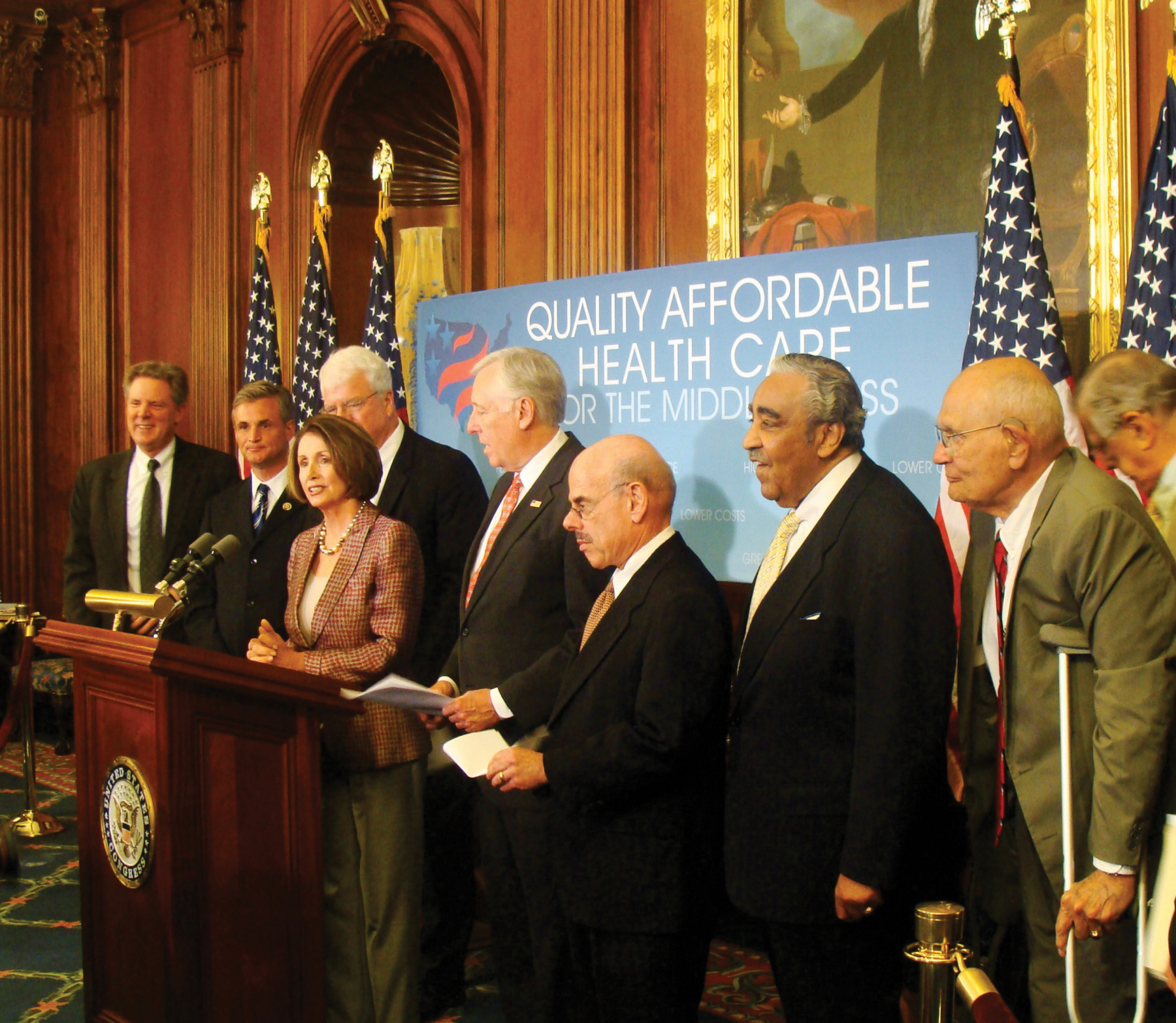 Photo of Nancy Pelosi at a podium, flanked by members of the House.