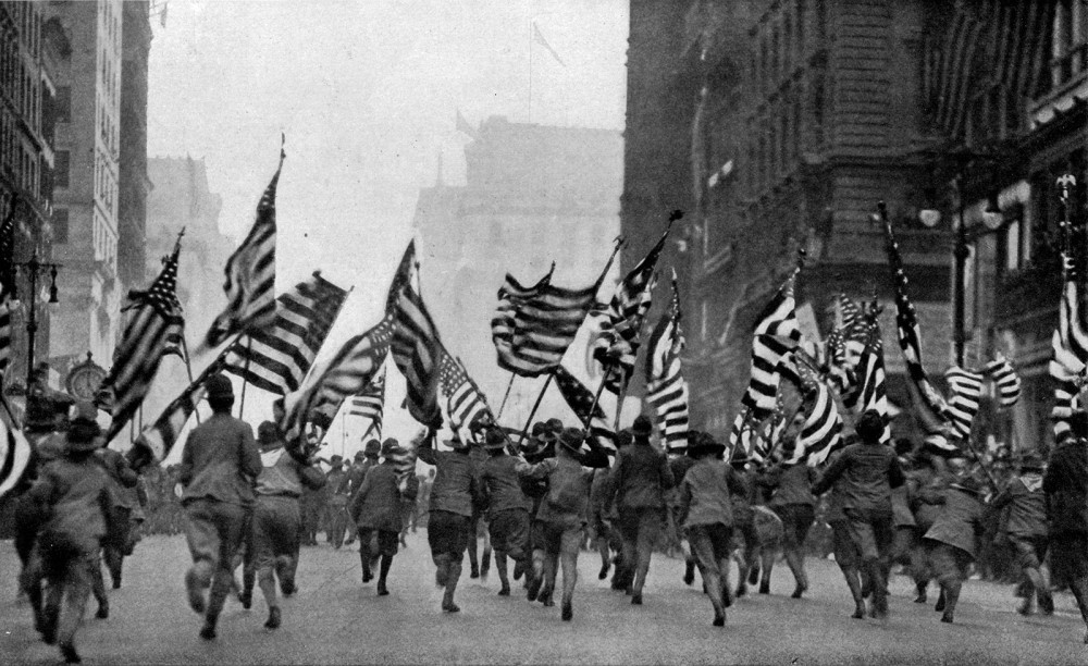 A crowd of people running down the street while holding America flags.