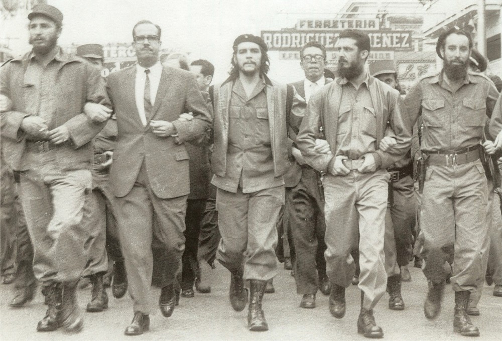 Photograph of a line of Cuban men with their arms linked. Two of the men are Fidel Castro and Che Guevara.