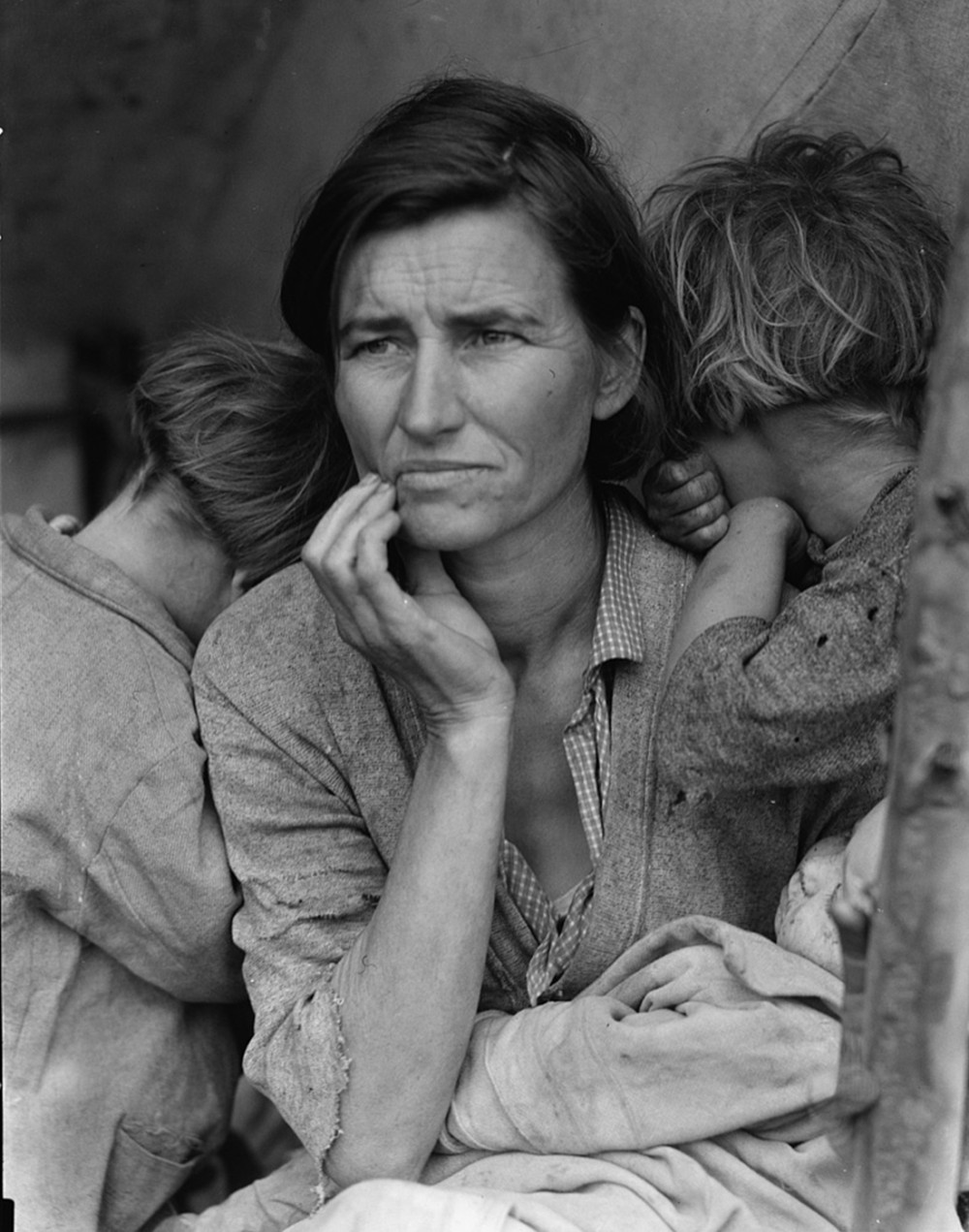 A woman looks off into the distance. Two children are burying their faces in her shoulders.