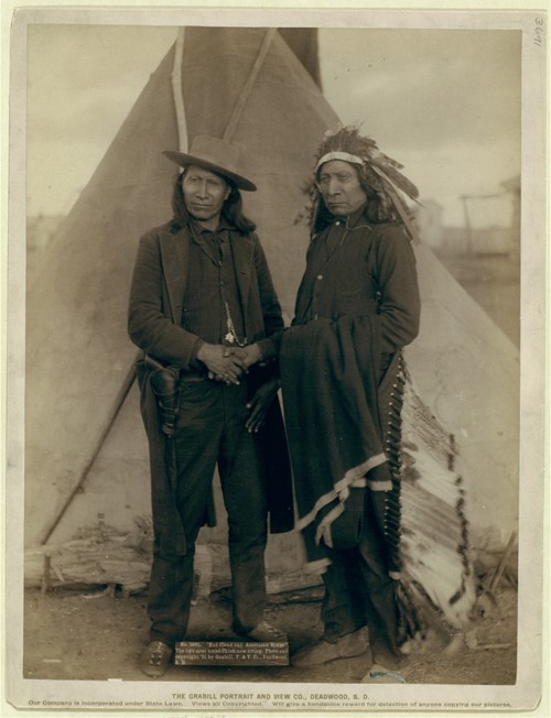 Red Cloud and American Horse, in Western-style clothing, shake hands.