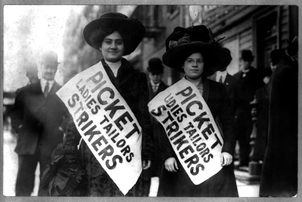 Two women wearing banners that say Picket Ladies Tailors Strikers.