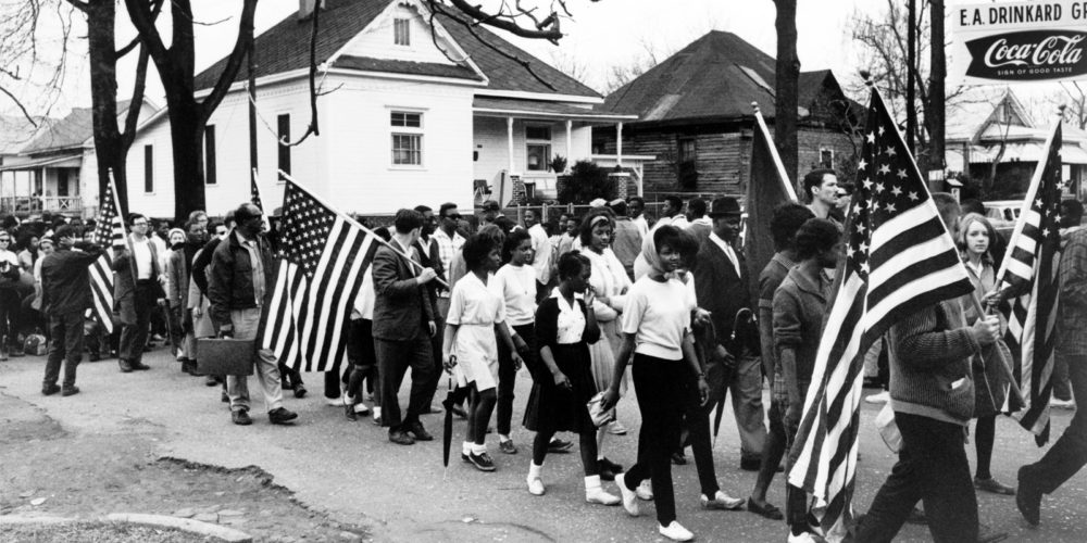 Protestors, mostly African-American, carry American flags and walk through the street.