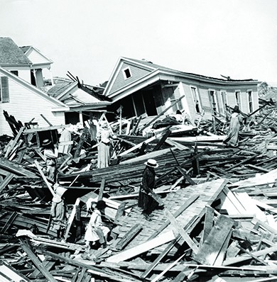 A photograph shows the devastation of the 1900 hurricane in Galveston, Texas. Residents climb among the massive woodpiles from fallen homes. Several other crushed houses are visible in the background.