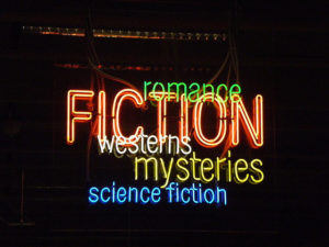 Neon sign with Fiction in red, all caps. Around it are smaller types of genres: westerns, mysteries, science fiction, and romance.