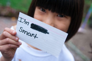 Girl holding an index card in front of her face, reading 