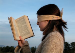 Woman wearing a blindfold, holding an open book up to her face