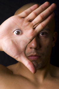 Photo of a man staring at the camera, with one palm covering half of his face. An eye is superimposed on his palm, roughly where it would be behind his hand in real life.