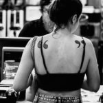 Black and white photo of a woman wearing a halter top, revealing quotation marks tattooed on each of her shoulderblades