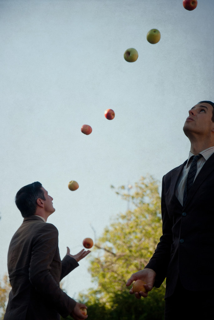Two men in suits, seen in profile, juggling apples.