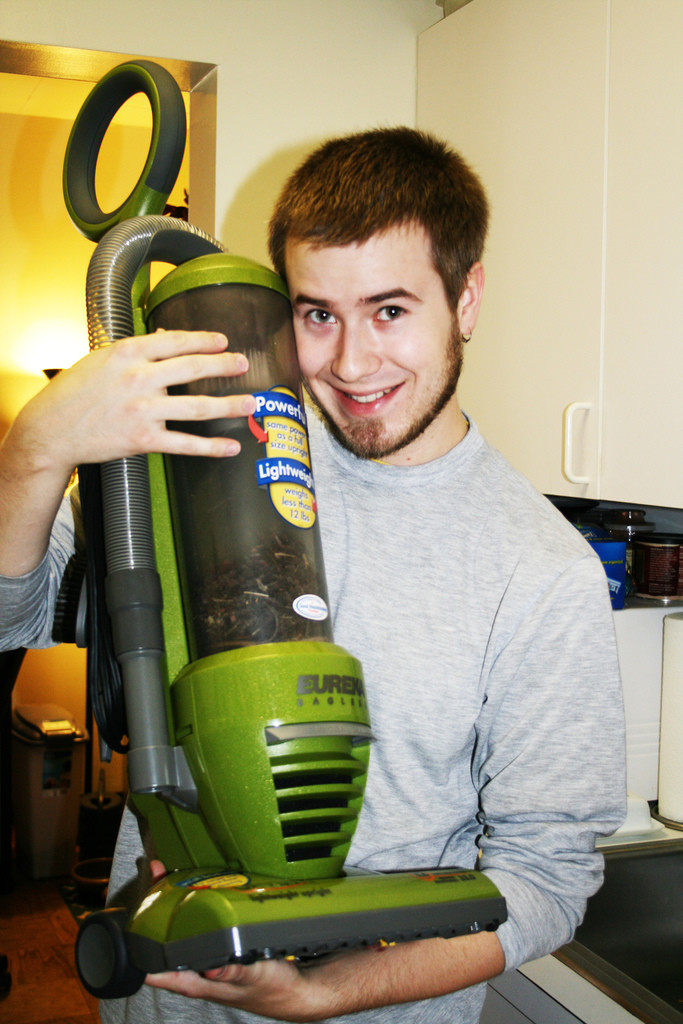 Young man holding a green vacuum cleaner and smiling