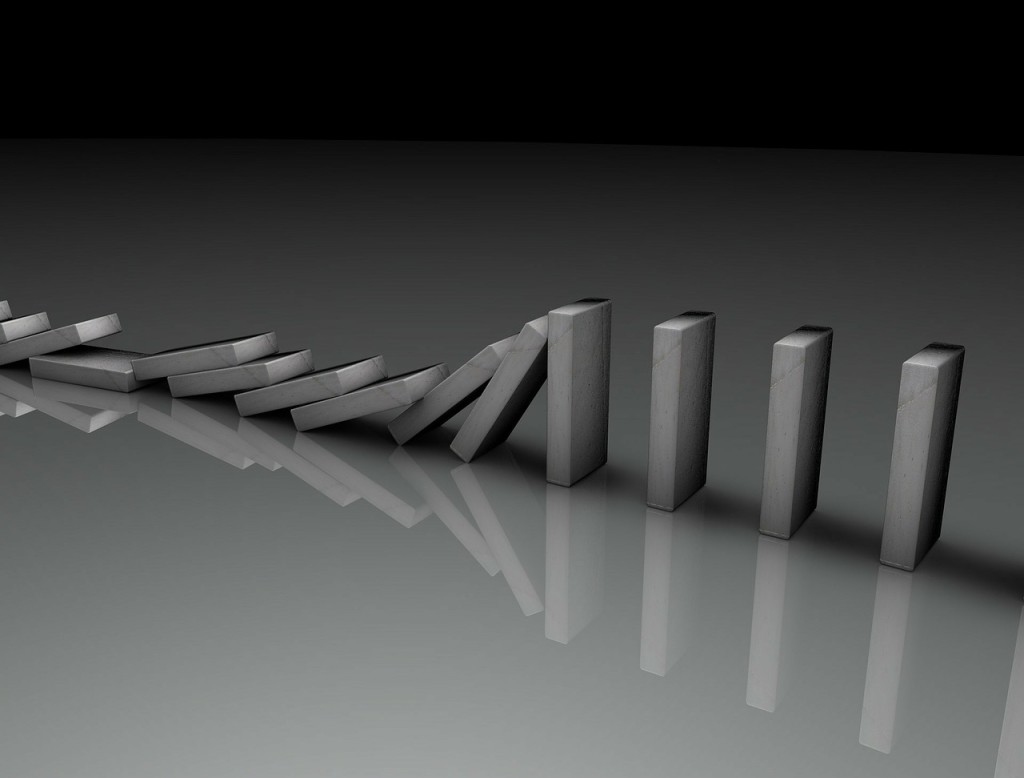 black and white photo of a line of gray dominoes. Ten have tipped over; six are still standing.