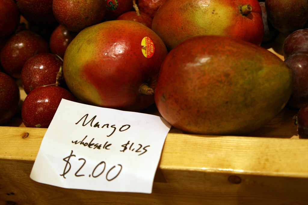 A basket of mangoes at the supermarket. A sign reads mango $2, wholesale $1.25.