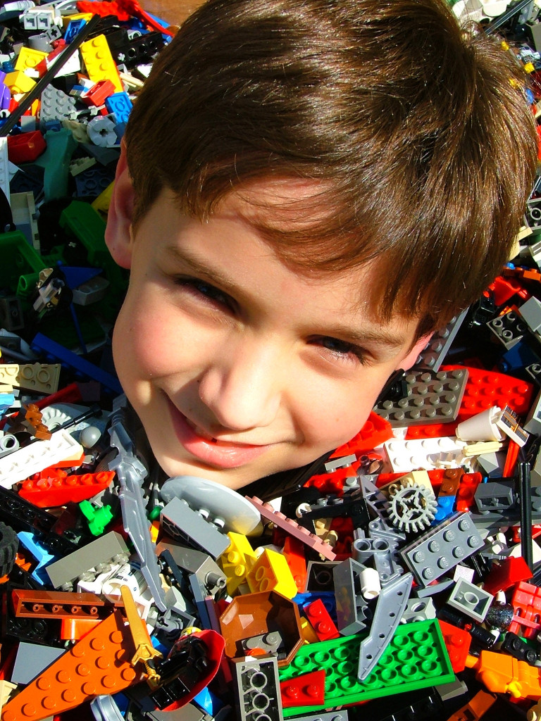 A photo of a young boy literally up to his neck in LEGOs.
