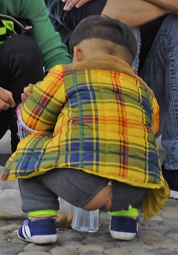 Chinese boy wearing open-crotch pants, squatting. His bare buttocks show in the center.
