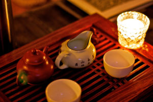 Two small teapots, two Chinese white teacups, and a votive candle sitting on a wooden tray