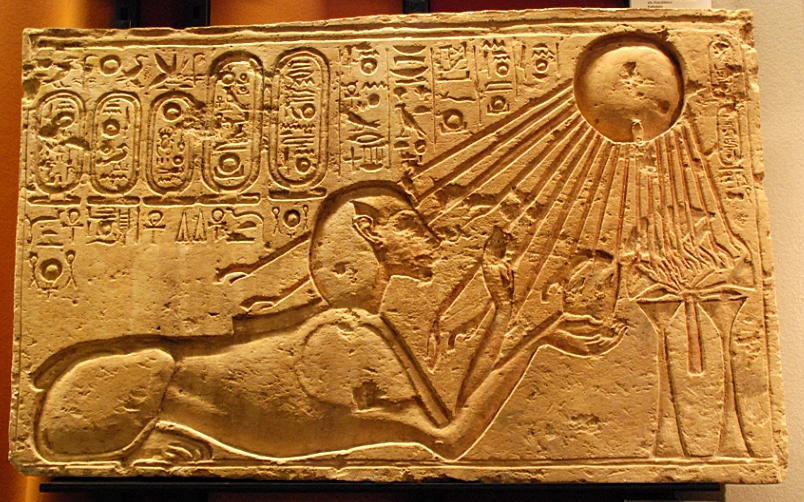 A carved stone relief of a sphinx under a sun, whose rays are shining onto the sphinx. Both are surrounded by hieroglyphics.