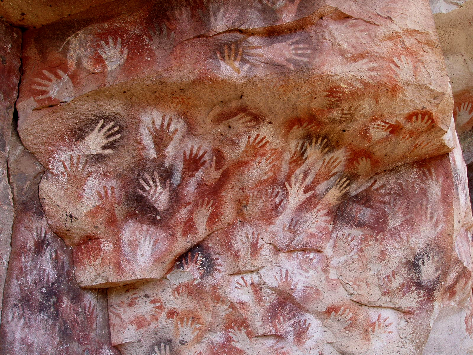 Photograph of Hands, at the Cave of the Hands. The cave painting appears as if the creators placed their hands on the wall and painted around them, leaving negative unpainted space where their hands once were.