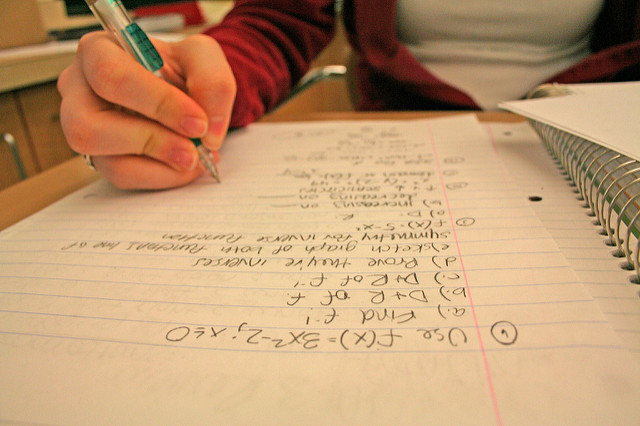 Close-up photo of a girl's hand writing math problems on notebook paper