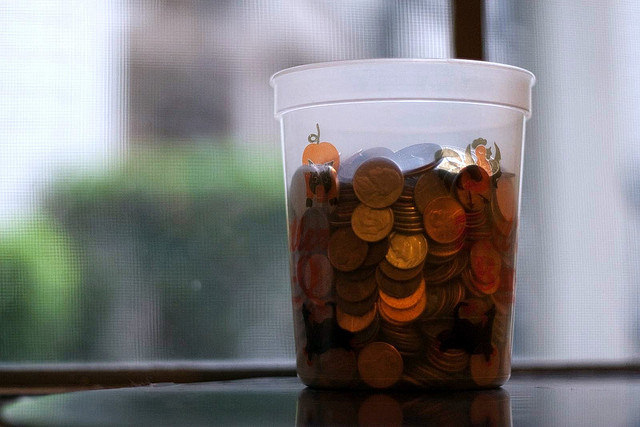 Plastic jar full of pennies sitting in front of a window